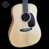 A close-up studio shot of an acoustic guitar against a solid black background, featuring a natural wood top, dark brown sides, and a dark tortoiseshell pickguard. A Tone Shop watermark is visible in the top-left corner.