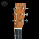 Close-up of the headstock of a Martin & Co acoustic guitar, showing the wood grain, six tuning pegs, and six strings against a black background.