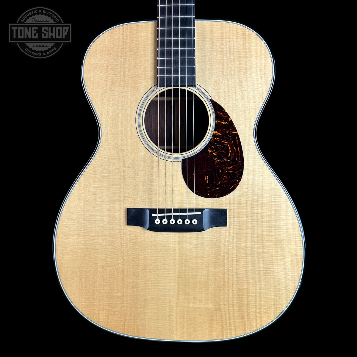 A front-facing acoustic guitar with a natural wood top, dark fretboard, and tortoiseshell-style pickguard on a black background. A Tone Shop watermark is visible in the upper left corner.