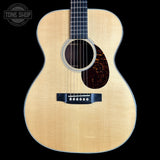 A front-facing acoustic guitar with a natural wood top, dark fretboard, and tortoiseshell-style pickguard on a black background. A Tone Shop watermark is visible in the upper left corner.