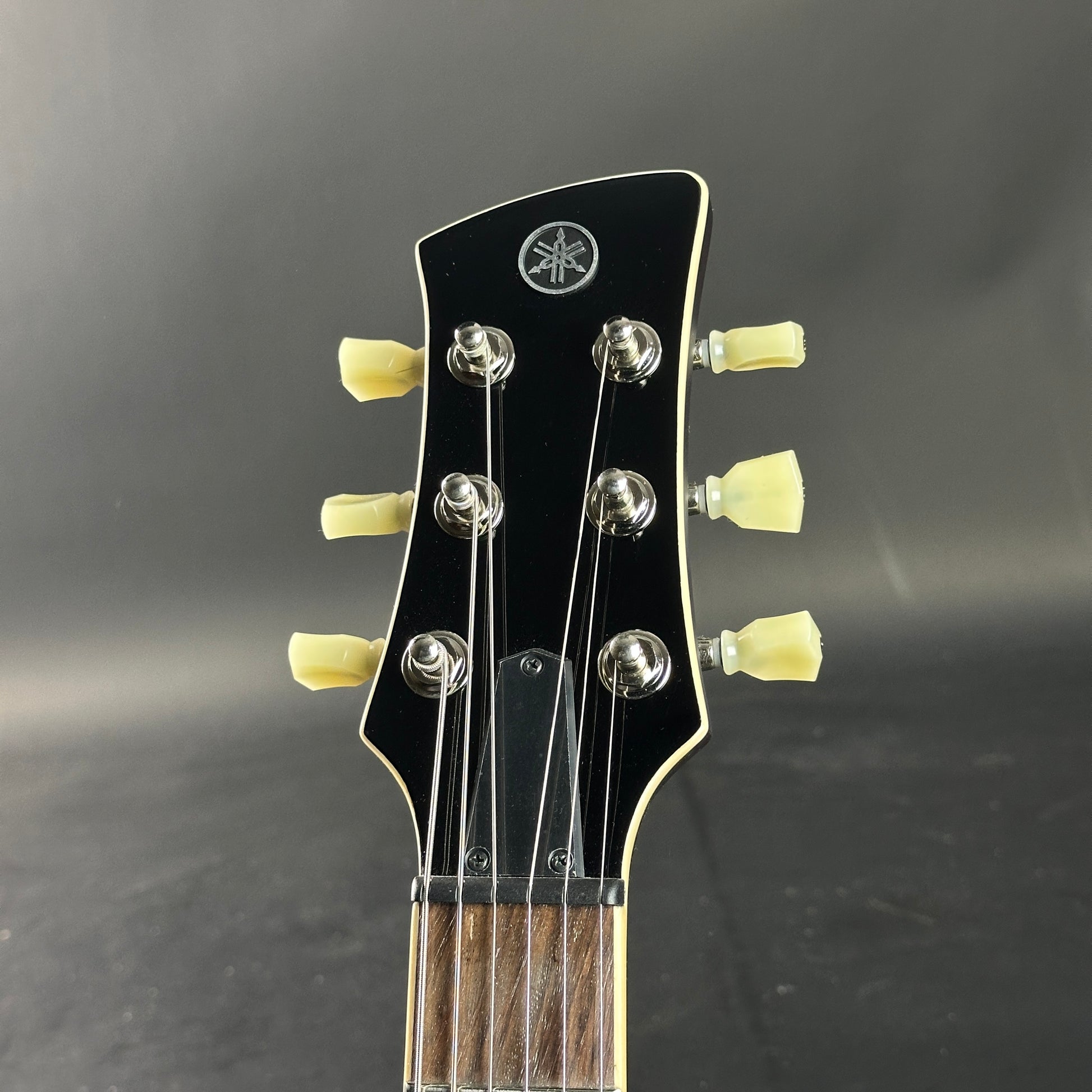 Guitar headstock with tuning pegs and brand logo on a dark background