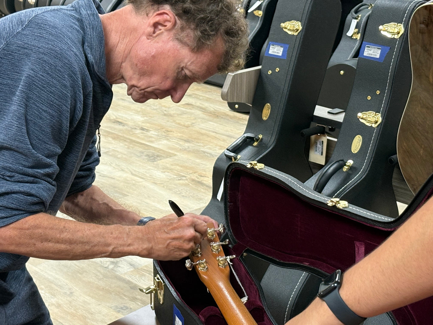 Person opening a guitar case with another person holding a guitar inside.