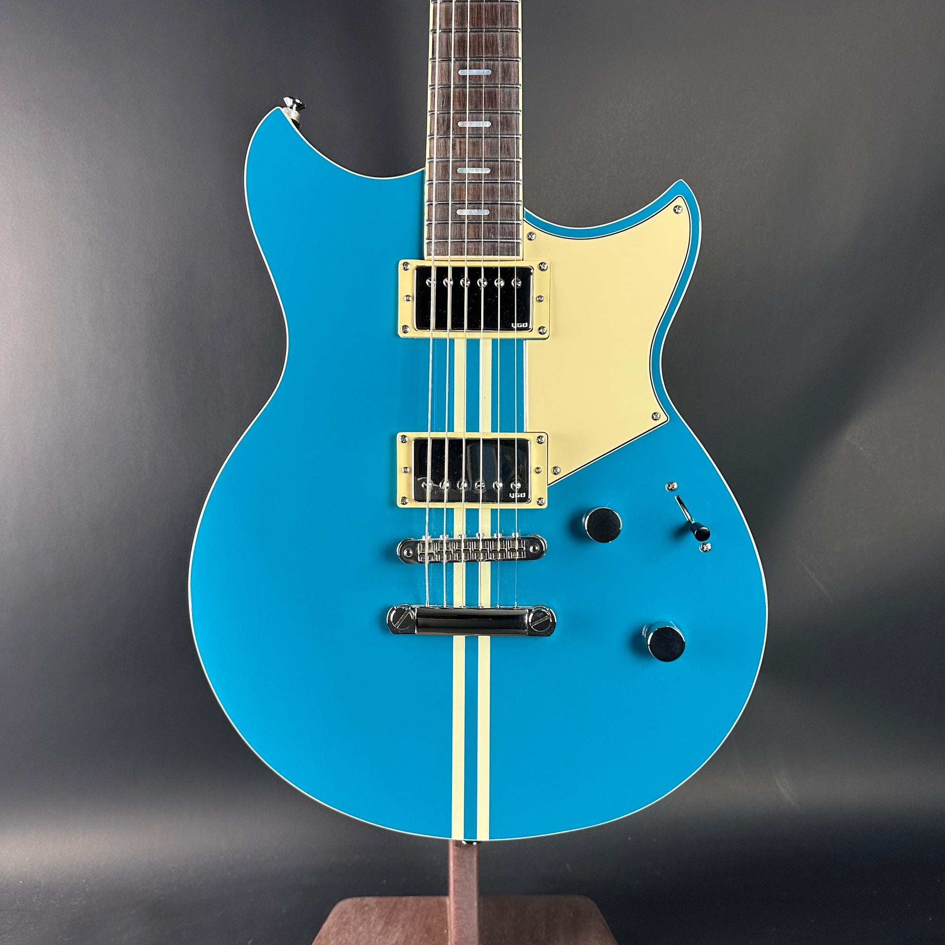 Blue electric guitar with a beige pickguard on a dark gray background