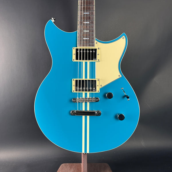 Blue electric guitar with a beige pickguard on a dark gray background