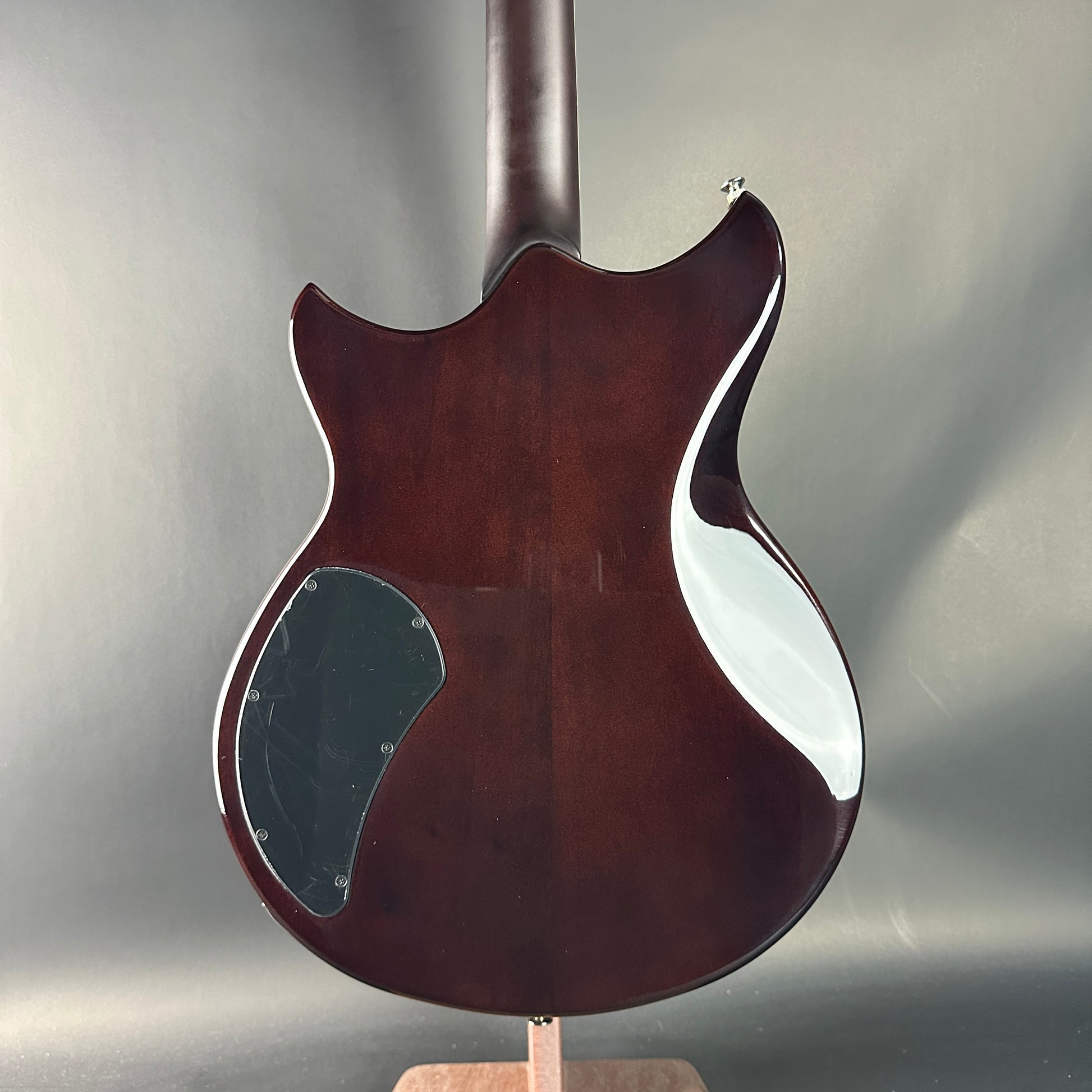 Back view of a wooden electric guitar on a stand with a gray background