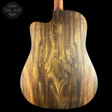 Close-up of the back of an acoustic guitar showing a rich, dark brown wood grain finish on a solid black background, with a Tone Shop watermark in the top left corner.