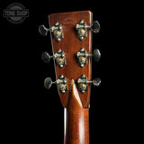 Close-up of the headstock of a guitar, showing six tuning pegs and the back of the wooden neck against a black background. A Tone Shop watermark is visible in the top left corner.
