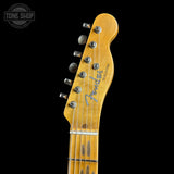Close-up of a Fender Telecaster electric guitar headstock in a natural maple finish, showing the six silver tuning pegs and Fender logo, set against a solid black background.