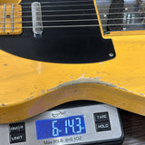 Close-up of a yellow electric guitar body resting on a digital scale to show its weight, with the scale displaying 6.143 lbs.