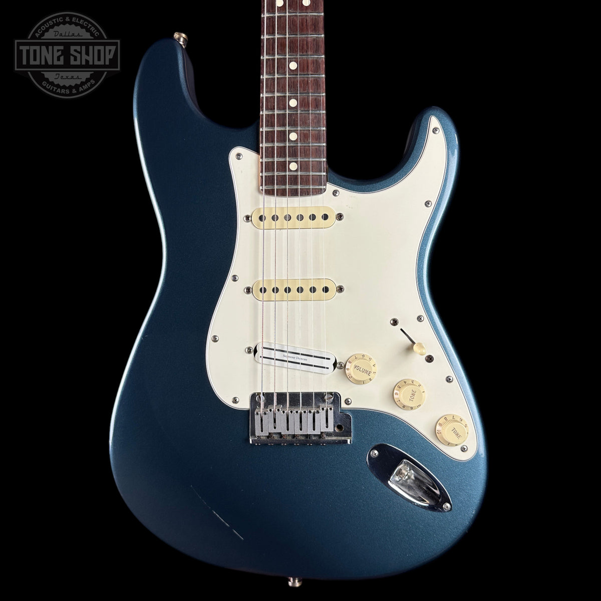Blue electric guitar with a white pickguard on a black background, featuring the Tone Shop logo.