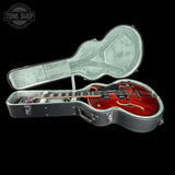 Red electric guitar in an open guitar case with 'Tone Shop' branding.