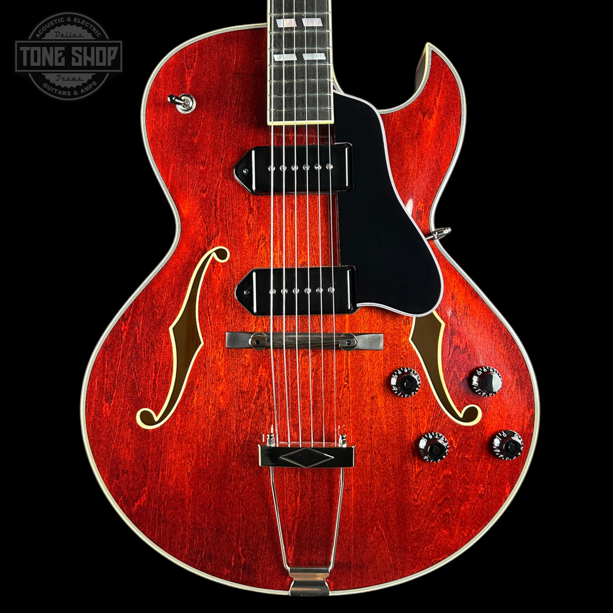 Red electric guitar with a black pickguard on a black background, featuring the Tone Shop logo.