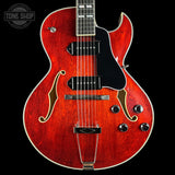 Red electric guitar with a black pickguard on a black background, featuring the Tone Shop logo.