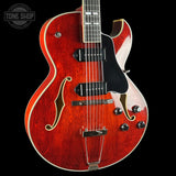 Red electric guitar with a black pickguard on a black background, featuring 'Tone Shop' logo.