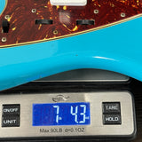 Digital scale displaying weight of a blue object next to a guitar neck
