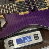 Purple electric guitar on a digital scale displaying weight.