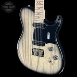 A close-up of an electric guitar with a natural wood grain finish, black pickguard, and black neck, shown against a solid black background. A Tone Shop watermark is visible in the top-left corner.