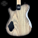 Close-up of the back of an electric guitar with a natural wood grain finish, black pickguard, and a black PRS Guitars logo plate on the neck joint, shown against a black background.