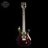 A classic electric guitar with a dark brown to black sunburst finish, featuring a double-cutaway body, maple fretboard, and gold-toned hardware, shown against a solid black background.