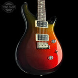 A classic electric guitar with a vibrant red-to-yellow-to-green gradient finish, shown against a solid black background. The brand logo on the headstock is not visible, but a 'TONE SHOP' watermark is in the top-left corner.