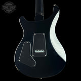The back of a black electric guitar with a glossy finish, featuring a white side strip, black pickguard, and silver hardware, shown against a black background with a Tone Shop watermark in the top left corner.