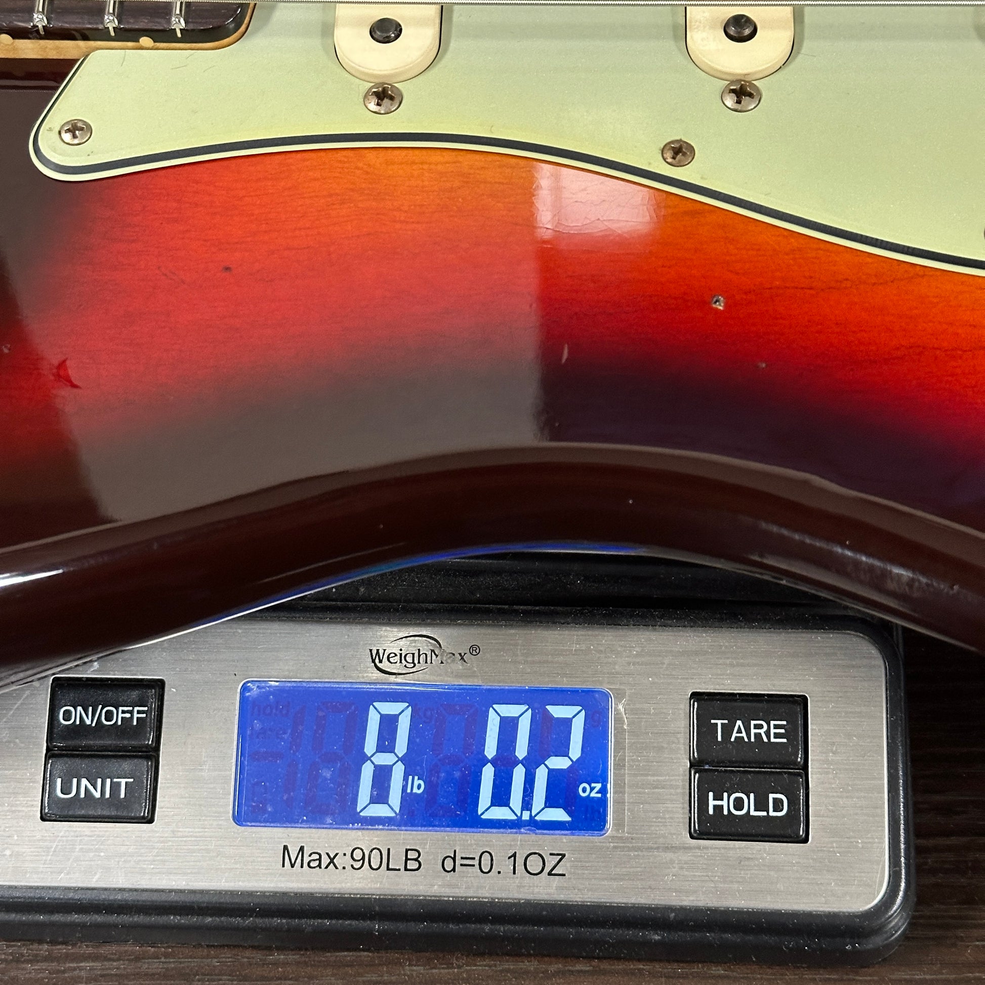 Digital scale displaying weight of a guitar, with a close-up view of the scale and guitar.