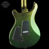 Close-up of the back of a glitter-finish electric guitar body in metallic green and gold, with black pickguard plates, shown against a black background. A Tone Shop watermark is visible in the upper left.