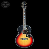 A classic acoustic guitar with a sunburst finish, featuring a black top, a warm orange-to-yellow center, and a red edge. It has ornate black pickguard details, a white binding, and a headstock with blue inlays.