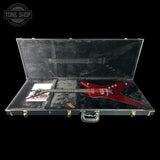 A red electric guitar displayed inside an open black hard case on a black background, with a Tone Shop logo watermark in the top left corner.