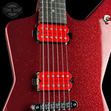Close-up of a red glitter electric guitar body with two bright red humbucker pickups, black hardware, and a dark fretboard on a black background. A Tone Shop watermark is visible in the top-left corner.