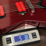 A close-up of a red glitter electric guitar body with red pickups, shown resting on a digital scale displaying 9.38 lbs.
