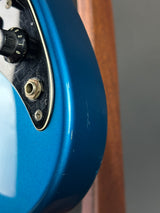 Close-up of a blue guitar headstock with tuning pegs on a wooden surface.