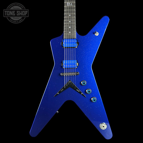 A blue sparkle electric guitar with a distinctive angular body, shown against a solid black background. The guitar features blue humbucker pickups, silver hardware, and a dark fretboard.