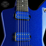 Close-up of a blue electric guitar body with two bright blue humbucker pickups and a black fretboard, shown against a black background. A Tone Shop watermark is visible in the top left.
