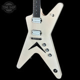 An electric guitar with a distinctive angular V-shaped body in a metallic champagne finish, featuring black hardware and pickups, set against a solid black background.