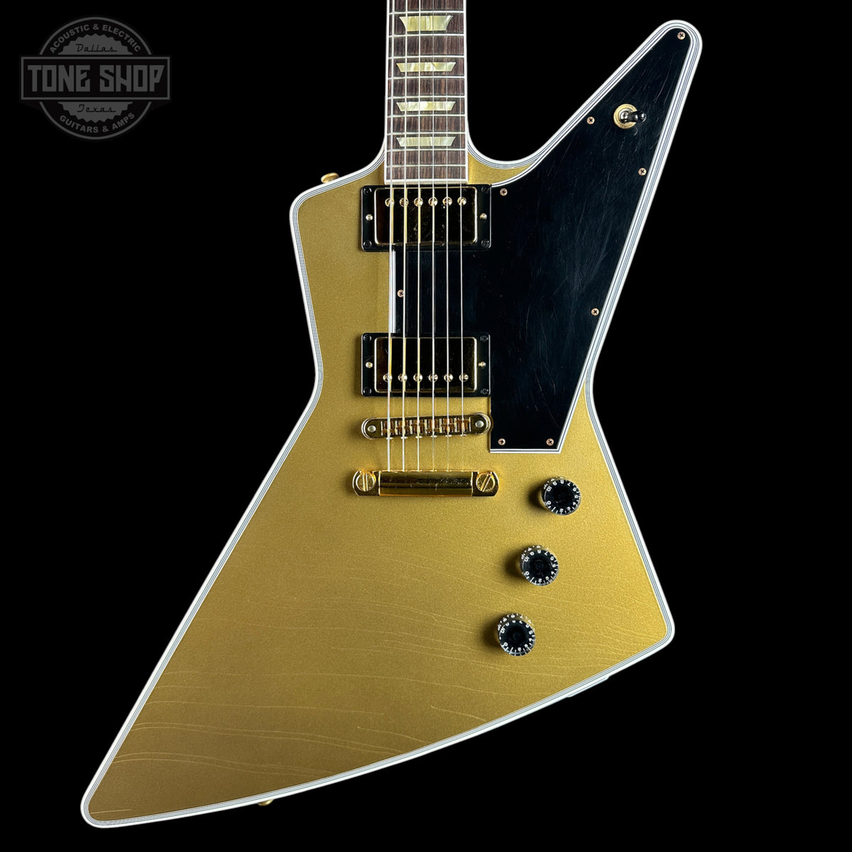 Gold electric guitar with a black pickguard on a black background, featuring 'Tone Shop' branding.