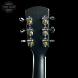 Close-up of the headstock of a black electric guitar, showing six tuning pegs with gold and silver details, set against a solid black background with a Tone Shop watermark in the top left corner.