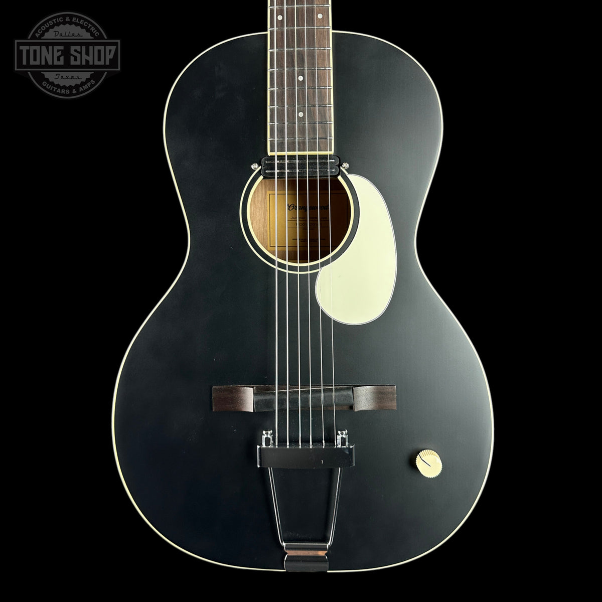 A black acoustic guitar with a glossy finish, featuring a cream pickguard, a dark wood fretboard, and a gold-toned tailpiece, shown against a solid black background.