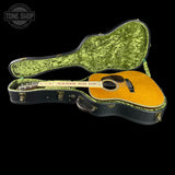 An acoustic guitar with a natural wood body and white fretboard displayed inside an open black hard case with a green velvet interior, set against a solid black background. A 'TONE SHOP' logo watermark is visible in the top-left corner.
