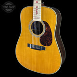 A close-up studio shot of a wooden acoustic guitar against a solid black background, featuring a natural golden-yellow spruce top, dark brown sides, and a black pickguard. The neck has red lettering that reads 'ECHO HOP FAY'.