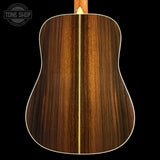The back of an acoustic guitar with a rich dark brown wood grain finish and a light cream-colored edge trim, shown against a solid black background.