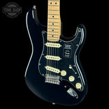 A black Fender Stratocaster electric guitar with a natural maple neck, featuring cream-colored pickups, a black pickguard, and gold-toned control knobs, shown against a solid black background.