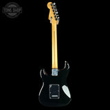 A black electric guitar shown from the back, featuring a natural maple neck, chrome hardware, and a silver plate on the body, set against a solid black background.