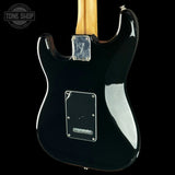 The rear view of a black electric guitar with a maple neck, featuring a glossy black finish, chrome hardware, and a white pickguard on a black background.