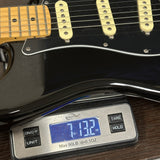 A close-up of a black electric guitar body with cream pickups and a maple neck, resting on a digital scale showing 7.132 oz.