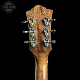 Close-up of the headstock of a wooden acoustic guitar, showing six tuning pegs with decorative gold and silver hardware, set against a solid black background with a Tone Shop watermark in the top left corner.