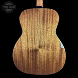Close-up of the back of a wooden acoustic guitar body, showing natural wood grain and a glossy finish, set against a solid black background with a Tone Shop watermark in the top left.