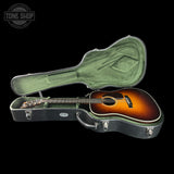 Acoustic guitar in a hard-shell case with 'Tone Shop' logo in the corner.