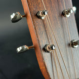Close-up of the headstock of a wooden acoustic guitar, showing six tuning pegs and strings against a dark background.