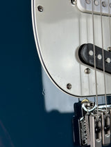 Close-up of a guitar's headstock with a brand name on a blue background